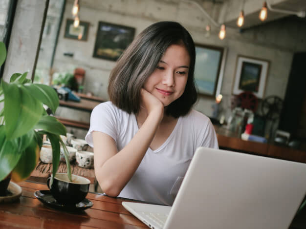 mulher com o rosto apoiado na mão usando o notebook