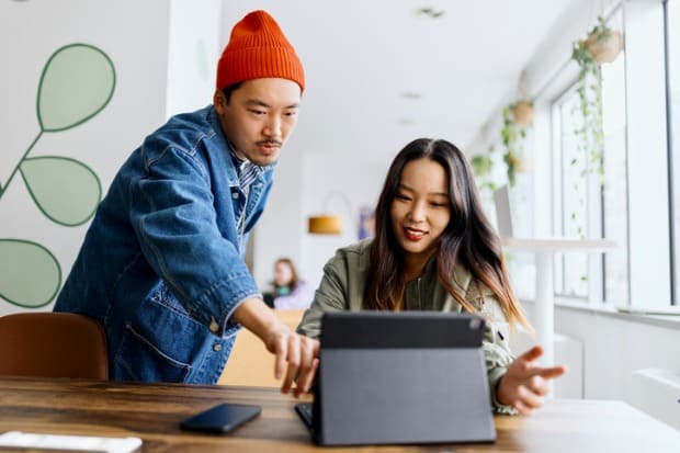 rapaz auxiliando moça no primeiro emprego enquanto ele pesquisa algo no notebook